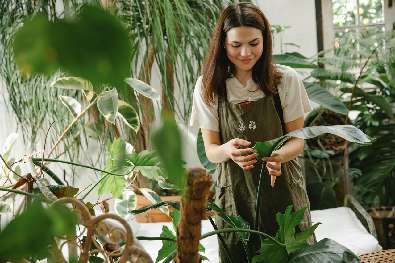 about-05 A woman in an apron tending to plants in a lush, sunlit greenhouse.